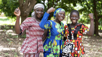 Group of young African villagers in colorful traditional dresses smiling at the camera. 